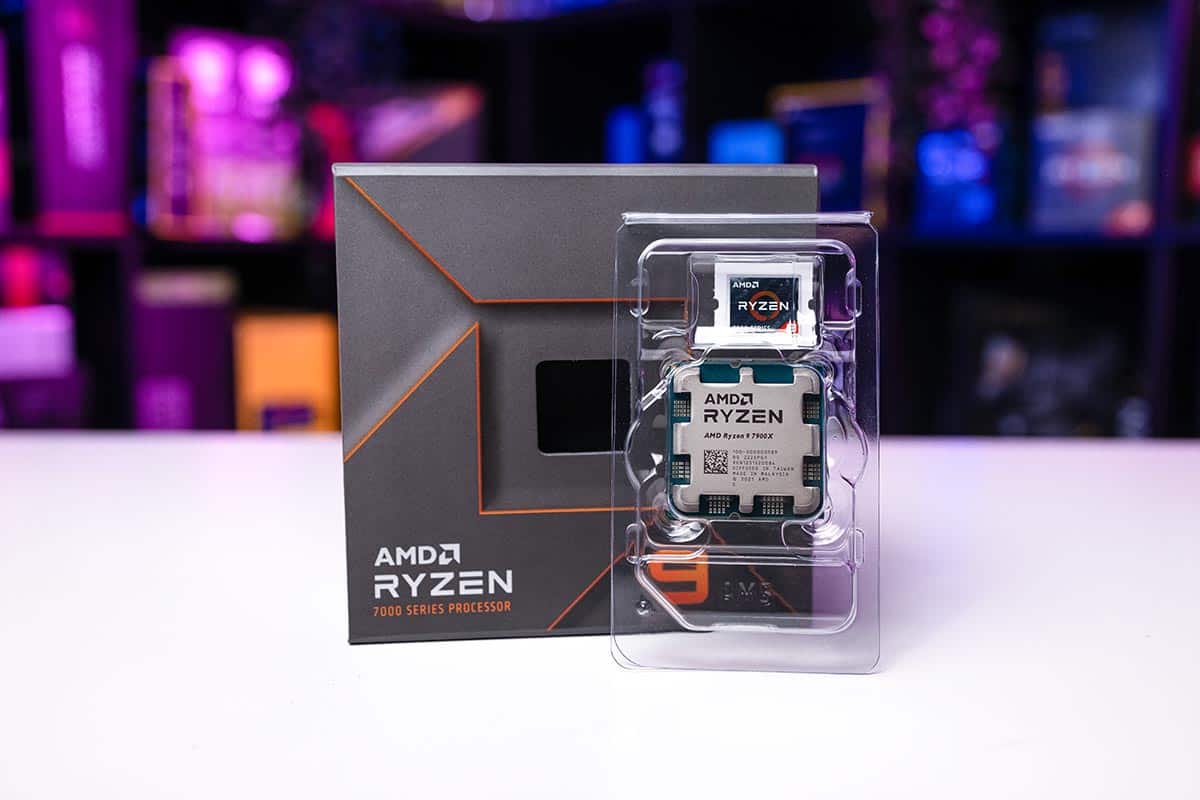 AMD Ryzen 9 7900X processor in a transparent case set beside its box on a table with a purple and pink lit background.