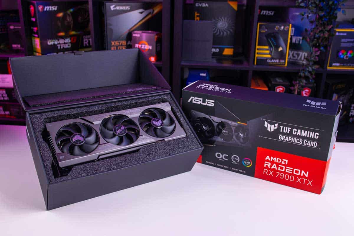 An Asus TUF Gaming Radeon RX 7900 XTX next to its packaging on a desk with computer hardware in the background.