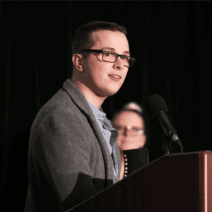 A man in glasses is giving a speech about us at a podium.