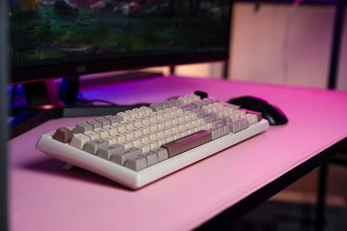 A retro-styled pink keyboard sits on a desk next to a monitor.