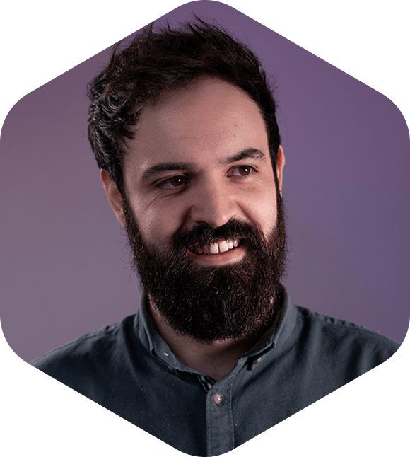 A man with a beard smiling in front of a purple background. About Us.