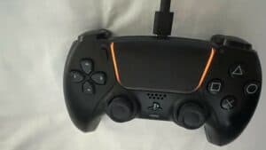 Connect a black and orange PlayStation controller to a white bed.