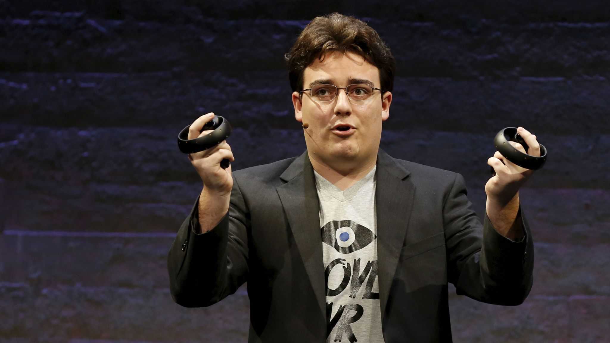 A man in glasses is holding up a pair of VR Headset headphones.