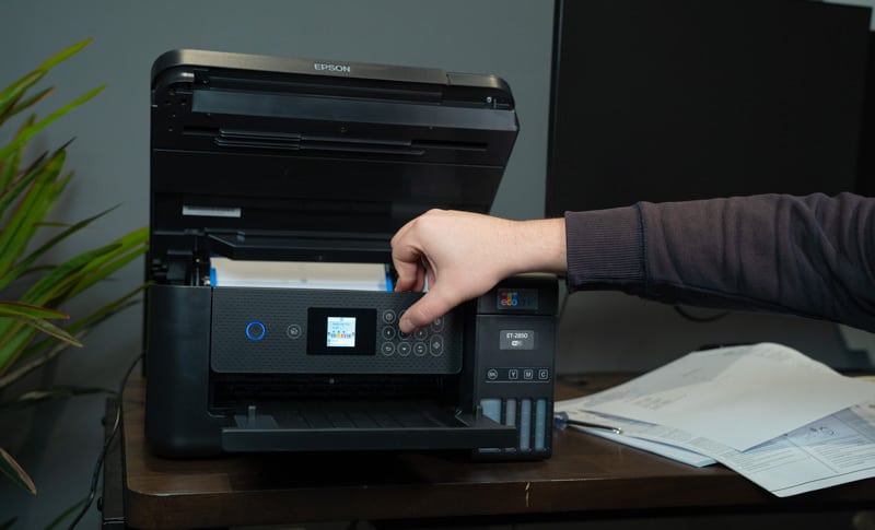 A person efficiently inserts a paper into an Epson EcoTank all-in-one printer, specifically the ET-2850.