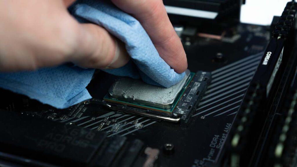 A person cleans thermal paste off a CPU on a motherboard using a blue cloth.