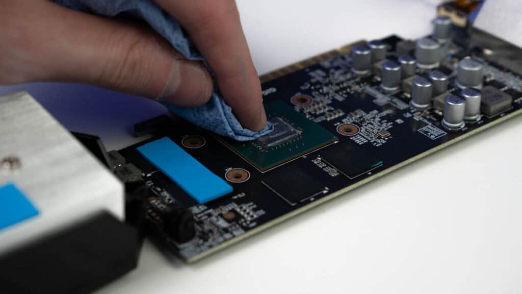 A person's hand applying thermal paste to a CPU on a computer motherboard using precise movements.
