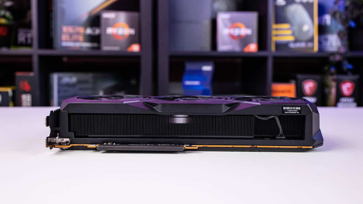 A graphics card, the AMD Radeon RX 7900 XT, with triple fans on a desk with gaming boxes in the background, truly worth it according to the latest review.
