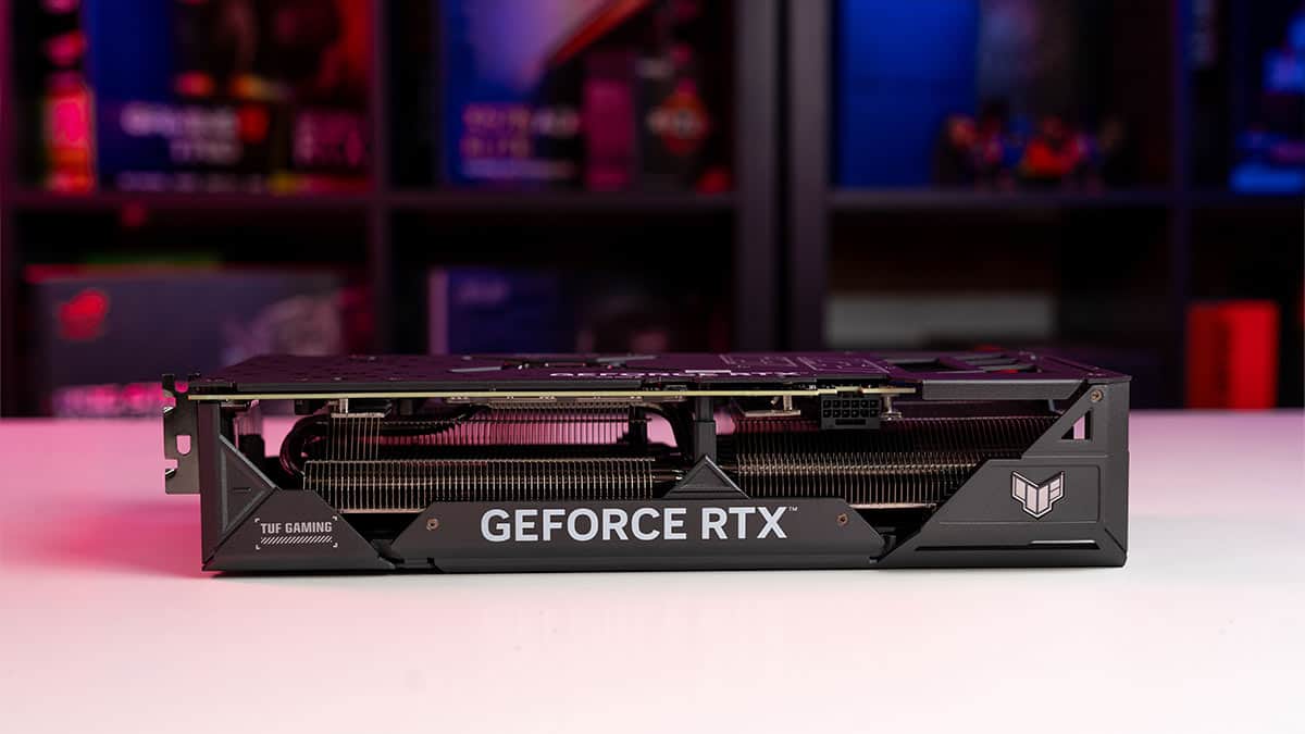 Nvidia GeForce RTX OC Edition graphics card from the TUF gaming series on a desk with a colorful, blurred background of bookshelves.