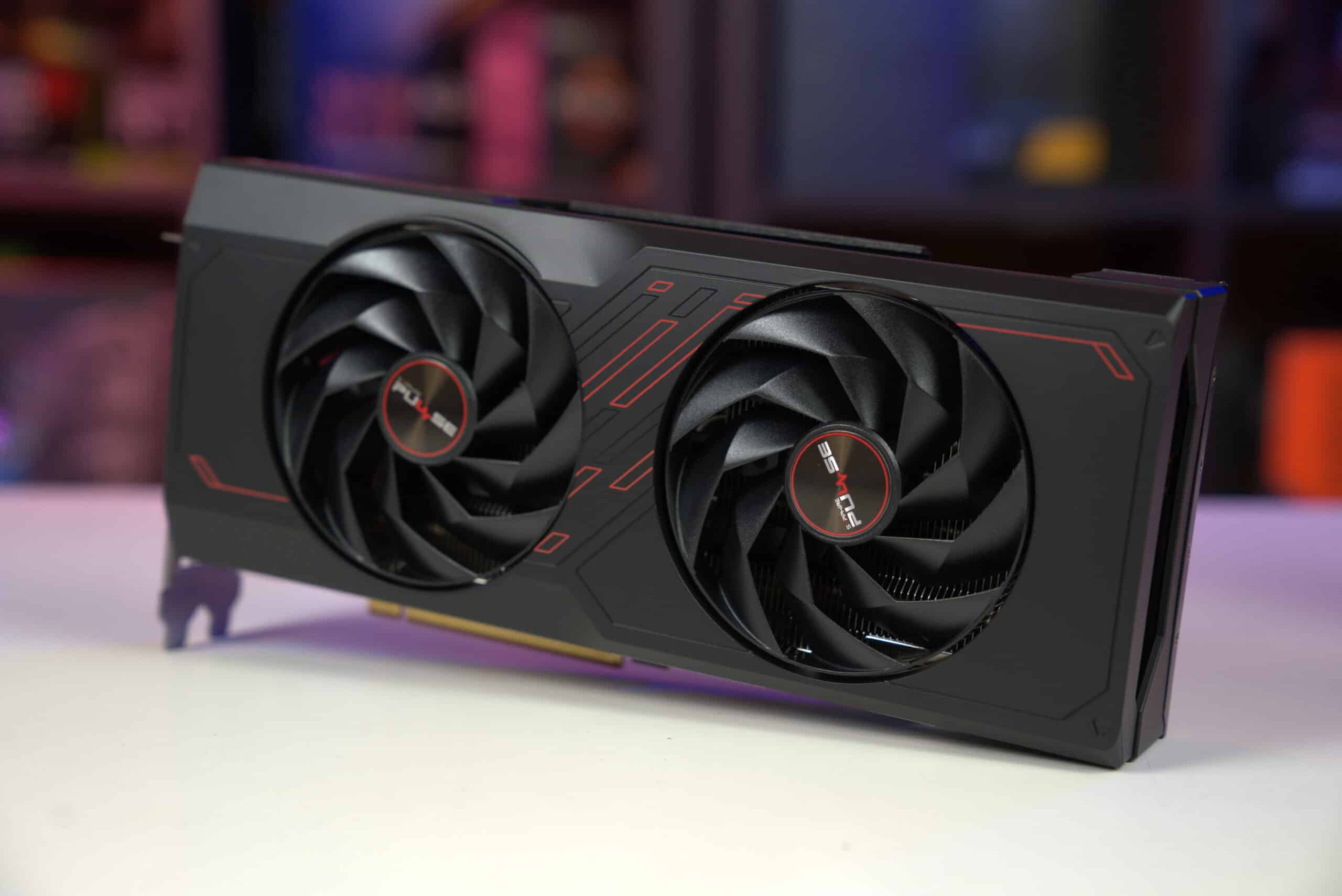 A high-performance RX 7700 XT dual-fan graphics card on a desk with a blurred background.