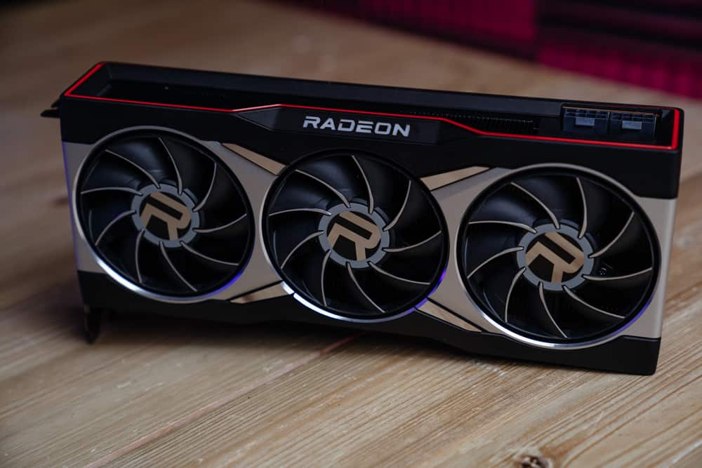 A triple-fan RX 7700 XT Radeon graphics card on a wooden surface.