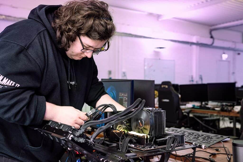 A person wearing glasses and a black hoodie is assembling computer components on a workbench for GPU testing.