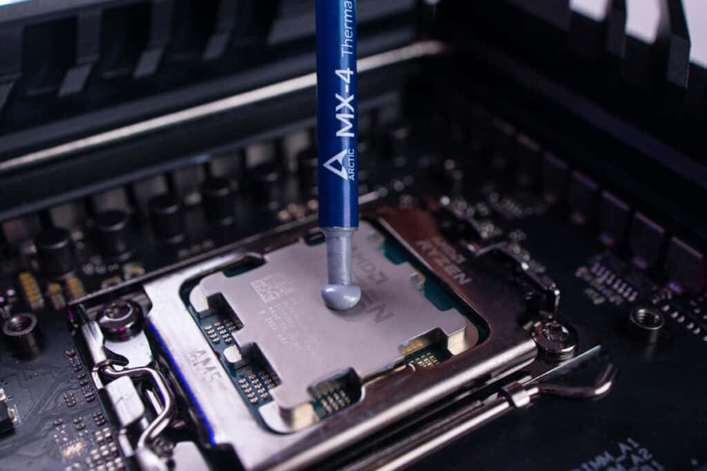 A tube of thermal paste being applied to a CPU on a motherboard to fix overheating.