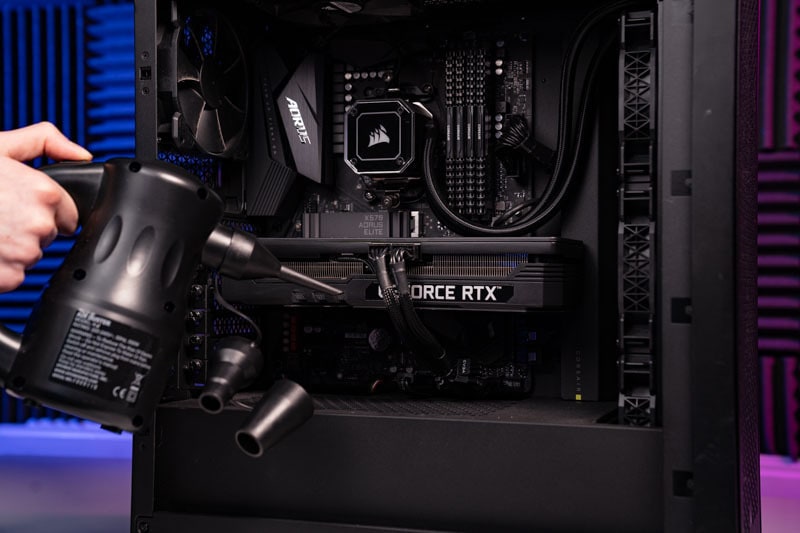 A person uses a portable vacuum to clean the interior of a computer case, focusing on a CPU and motherboard.