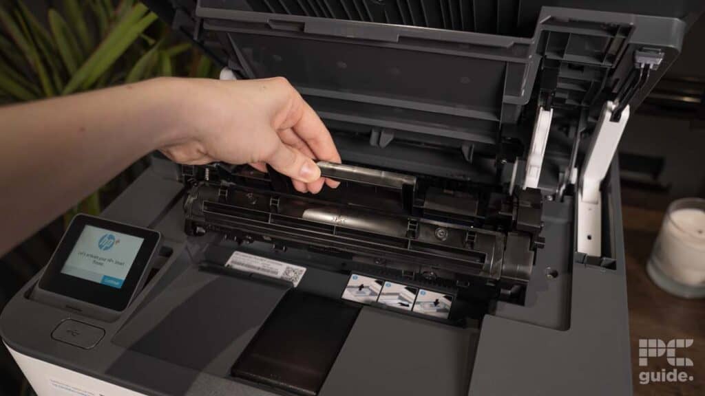 A person's hand replacing the toner cartridge in a modern HP LaserJet Pro MFP 3102fdwe printer.