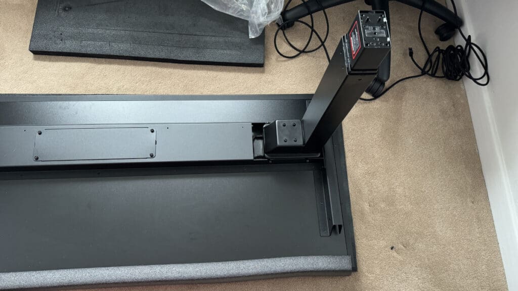 Partially assembled treadmill with scattered components and an electronic control panel on a Secretlab Magnus Pro carpeted floor.