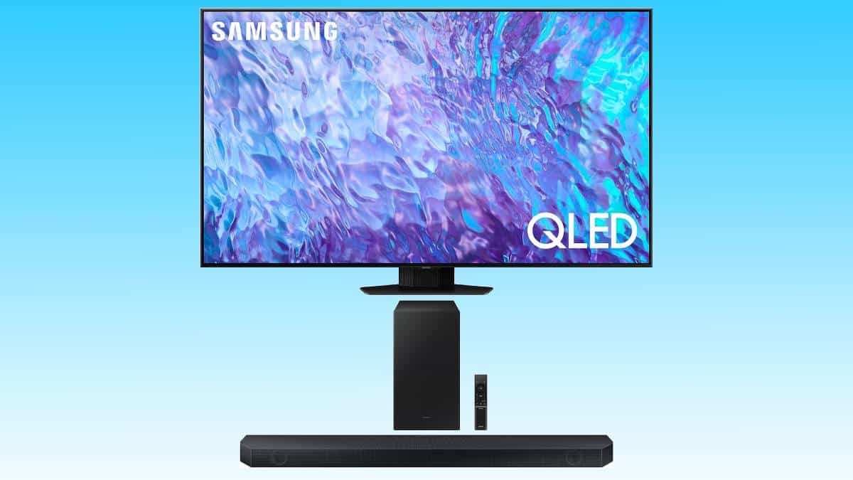 A Samsung QLED TV bundled with a soundbar, displaying an abstract blue and purple image, mounted on a stand with a remote in front.