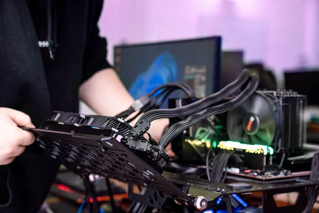 Person installing a graphics card into a computer setup for GPU benchmarking.