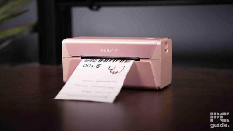 A pink Munbyn RW401AP label printer on a desk, printing a label with a barcode and text.