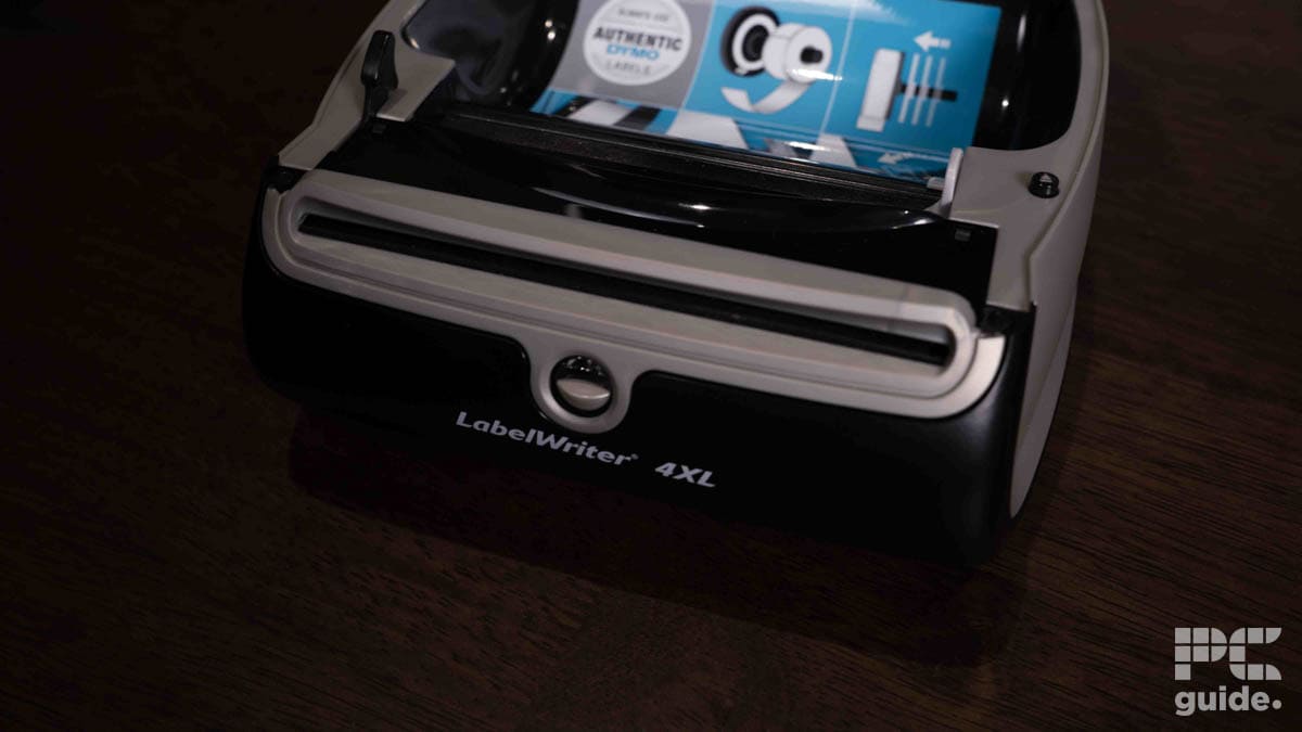 A Dymo LabelWriter 4XL printer on a wooden surface, displaying a label with a cartoon character on its screen.