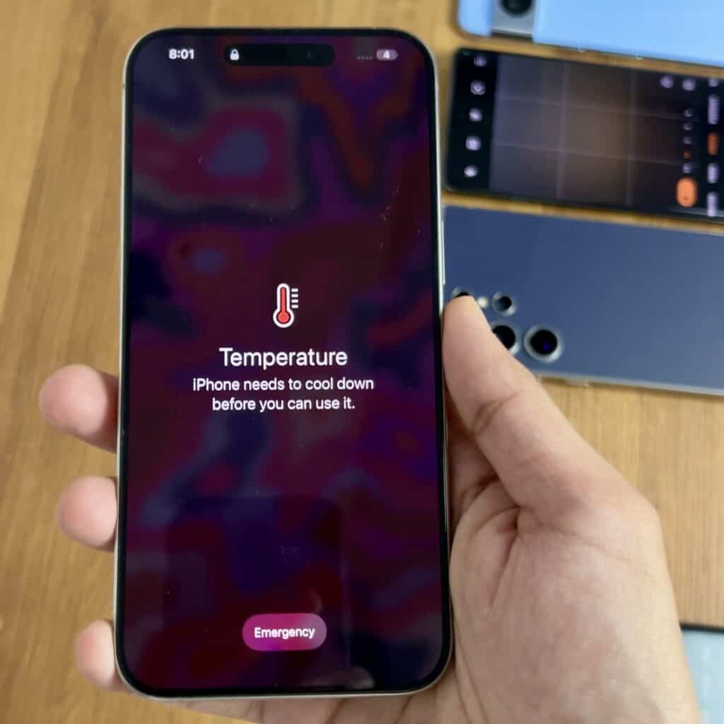 Hand holding an iphone showing a temperature warning on the screen, indicating that the phone needs to cool down before use.