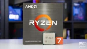 An AMD Ryzen 7 5700X processor box and chip from the 5000 series on a table, with a blurred background featuring computer equipment.