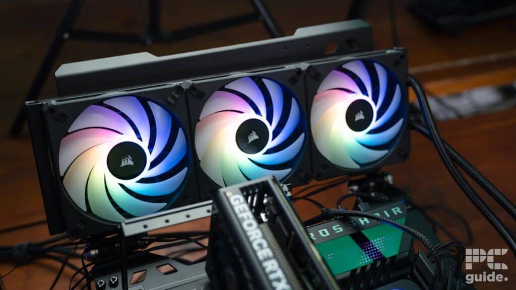 A computer setup with three cooling fans displaying colorful LED lights, a GeForce RTX graphics card, and a motherboard visible. For an in-depth look at the cooling system's performance, check out the Corsair H150i ELITE LCD XT review.