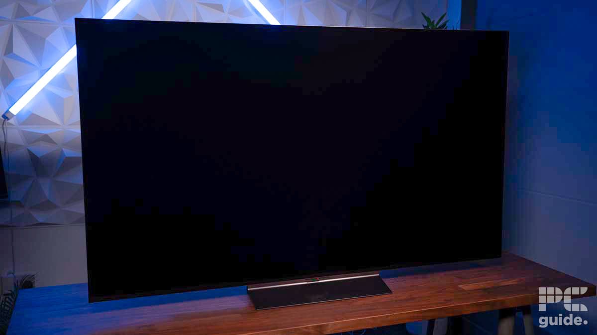 A flat-screen TV on a wooden stand with a geometric-patterned wall in the background. The TV screen is off, and a small 