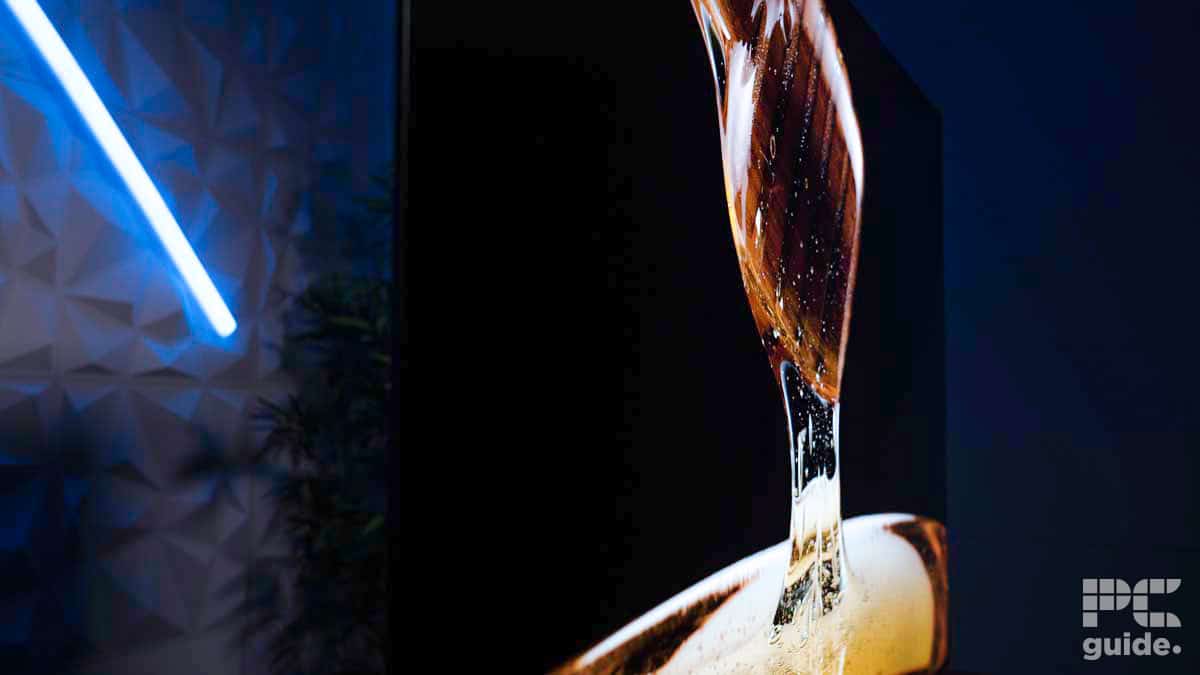 A close-up image of a modern, flat-screen TV, likely featured in an LG C4 OLED review, displaying a detailed, high-resolution image of a beverage being poured into a glass. A faint neon blue light is visible in the background on the left side.