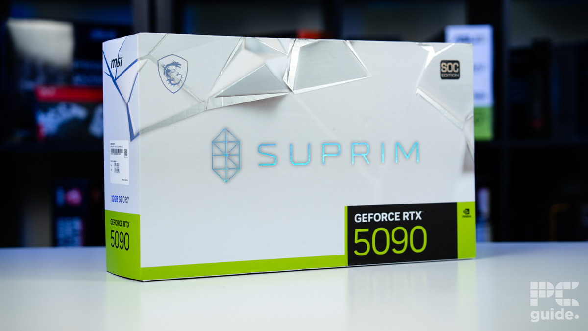 A background of blurred tech boxes sitting on bookshelves. The MSI Suprim SOC RTX 5090 box sits on top of a white table. It is a white box with the MSI logo in the top left, SOC edition top right, Suprim name and lgoo in the middle, and GeForce RTX 5090 name in the bottom right.