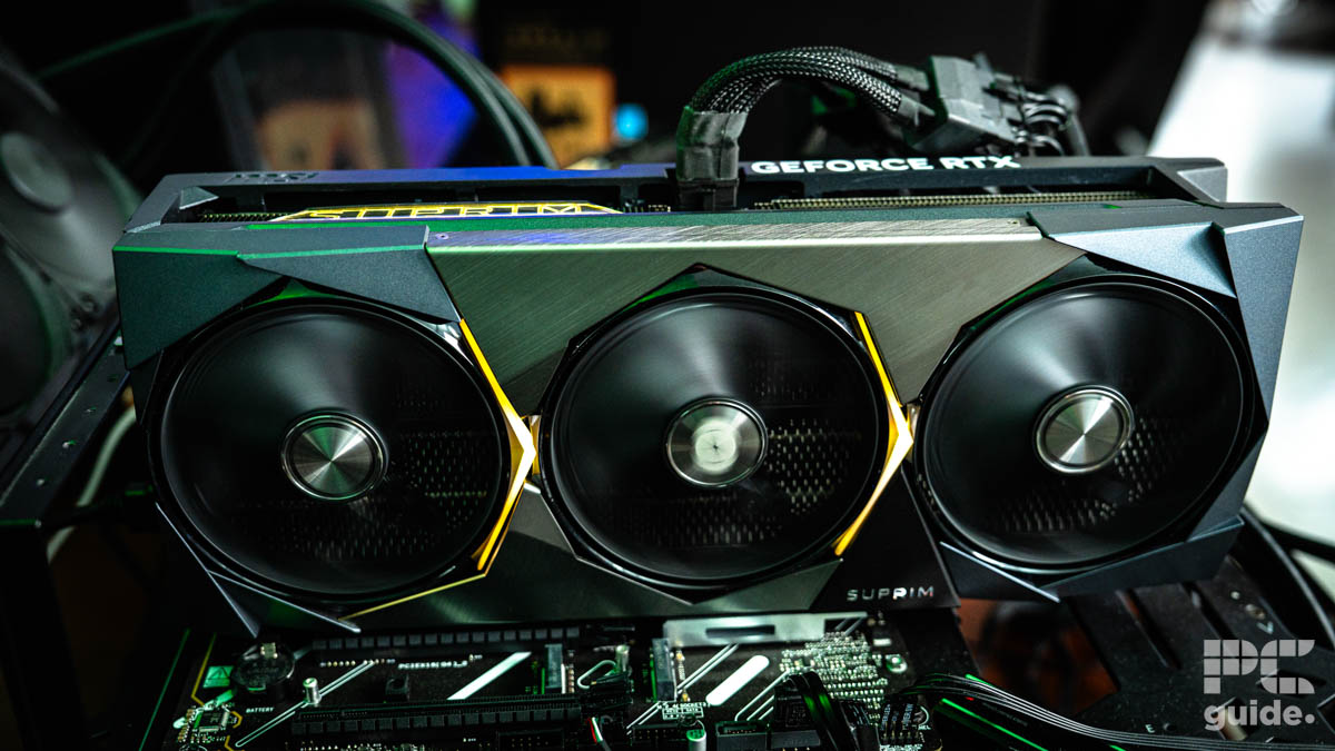 A silver GeForce RTX graphics card plugged into a motherboard and turned on. The three fans at the front of the card are spinning with teh adapter cable coming out the top.