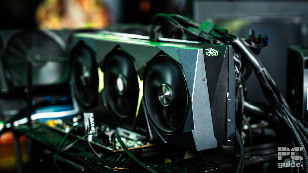 A silver GeForce RTX graphics card plugged into a motherboard and turned on. It's a shot from the front profile that shows the fans spinning, and RGB between them lit up in yellowish green. On the top is an adapter and there are fans behind it.