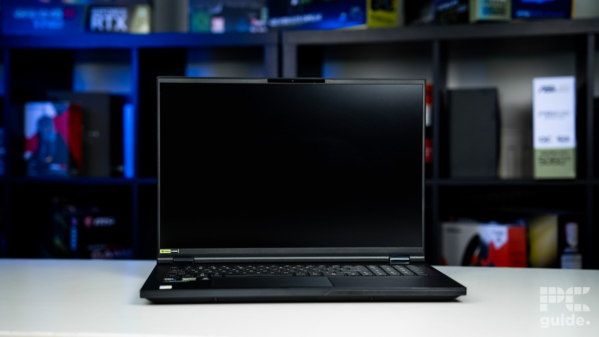 A black laptop with a black screen opened. Sitting on a white table with a blurred background of shelves filled with boxed of tech products.