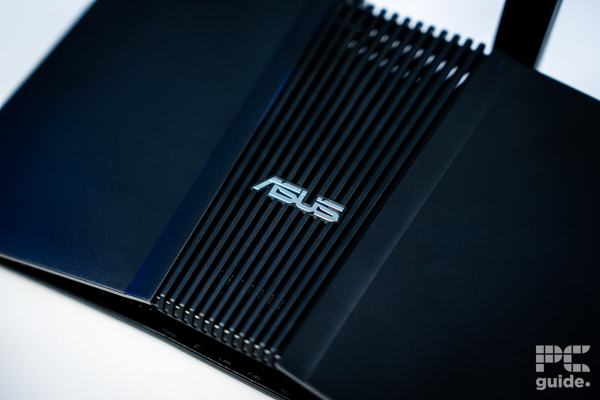 The black ASUS RT-BE58U (BE3600 router sitting on a white table. A close up of the middle plastic vents with the ASUS logo in the middle.