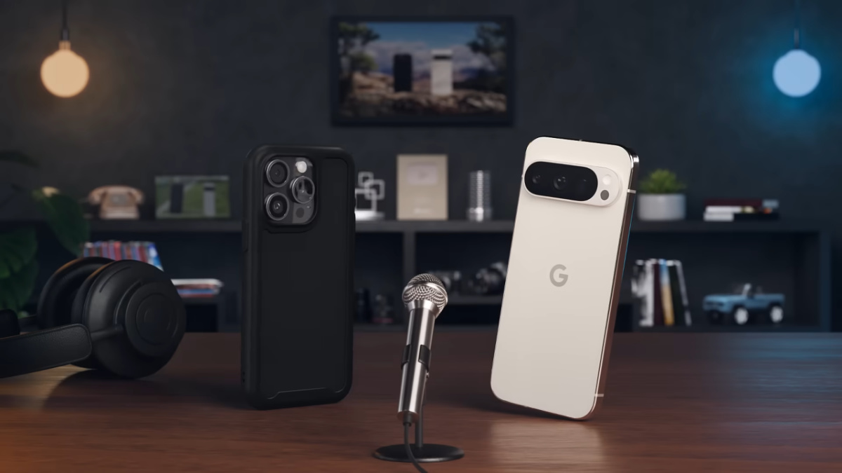 A black painted wall as a bakground with a framed photo top centre, and a booksheld spanning across the photo, with a yellow light in the top left, and a blue one in the top right. In the fore front is a table with a small microphone in teh centre on a stand with an iPhone in a case on the left and a Google Pixel 9 Pro on the right