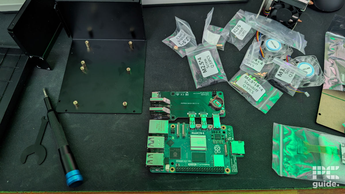 A mousepad filled with baggies of screws and standoffs. Along with a metal plate for the Pironman 5 Max case with standoffs installed. in between is a Raspberry Pi 5 plugged in with a HDMI adapter PCB.