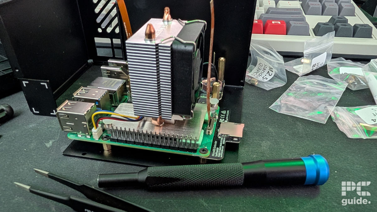 A Raspberry Pi 5 installed on the Pironman 5-Max case with a heatsink tower and fan. Next to it are a scattering of plastic baggies and tools.