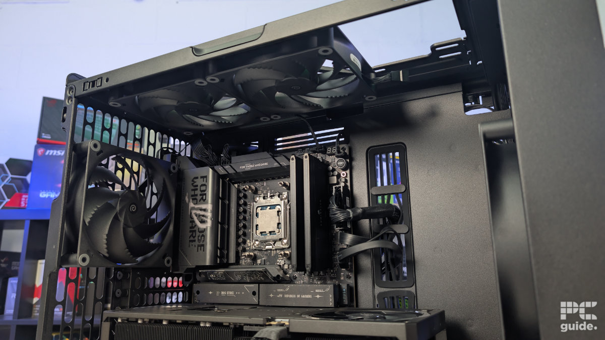 A inside view of the HAVN BF 360 case with the top taken off and a two 140mm fans installed. With the inside built wihth PC components, standing on a white desk with a background of PC component boxes on a bookshelf.