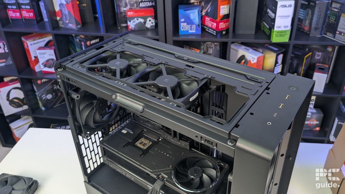 A top down view of the HAVN BF 360 case with the top taken off and a two 140mm fans installed. With the inside built wihth PC components, standing on a white desk with a background of PC component boxes on a bookshelf.