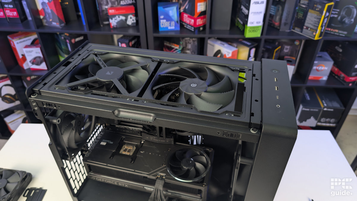 A top down view of the HAVN BF 360 case with the top taken off and a two 180mm fans installed facing opposite directions. With the inside built wihth PC components, standing on a white desk with a background of PC component boxes on a bookshelf.