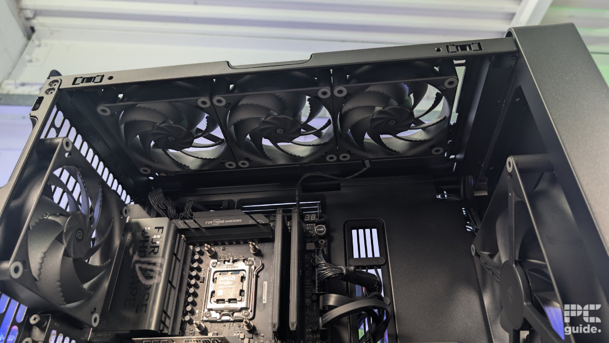 A inside view of the HAVN BF 360 case with the top taken off and a three 120mm fans installed. With the inside built wihth PC components, standing on a white desk with a background of PC component boxes on a bookshelf.
