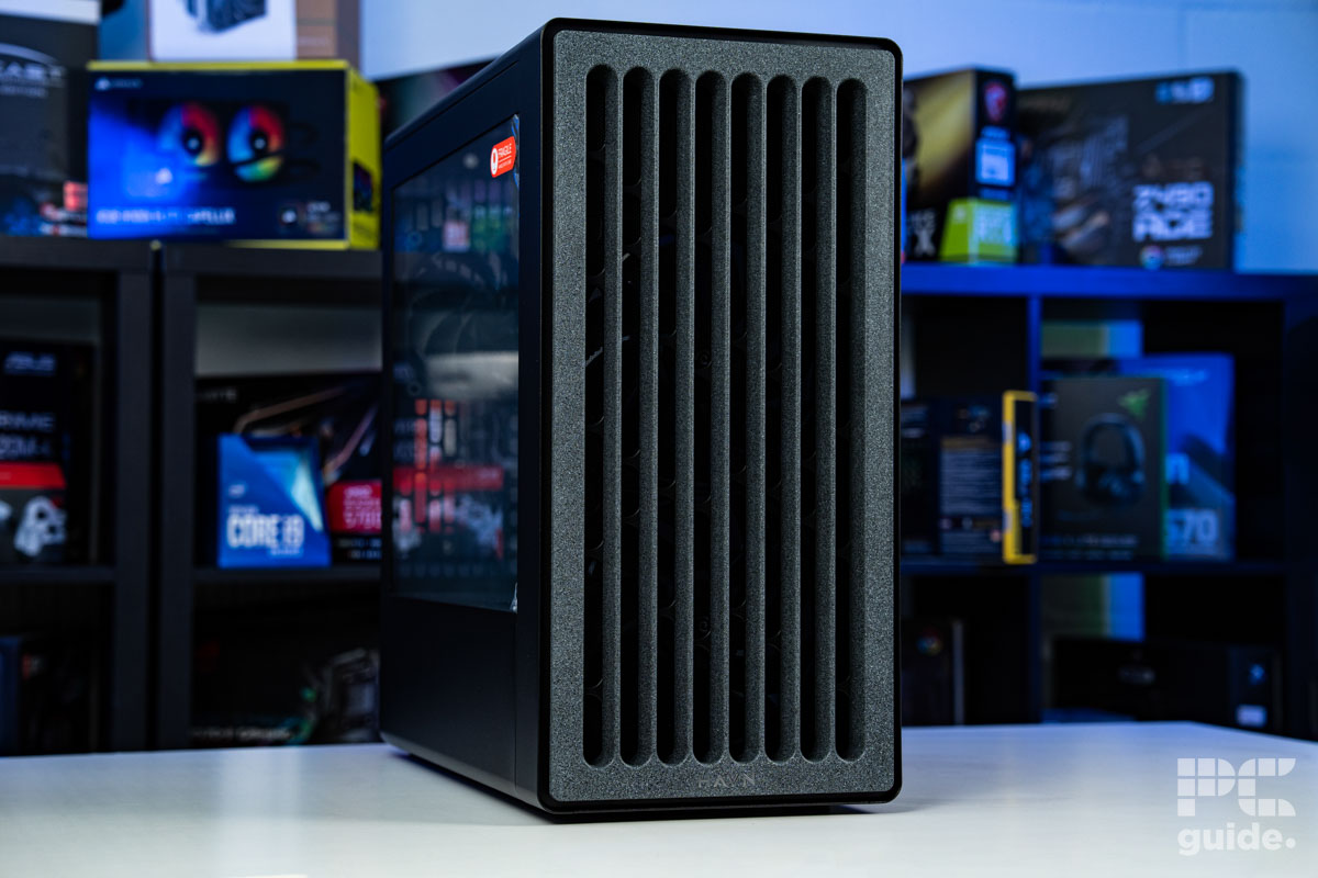 A shot of the fron of the HAVN BF 360 Flow case on a white table with a background of PC component boxes on a bookshelf. It has a faux stone looking design with vertical slits for airflow.