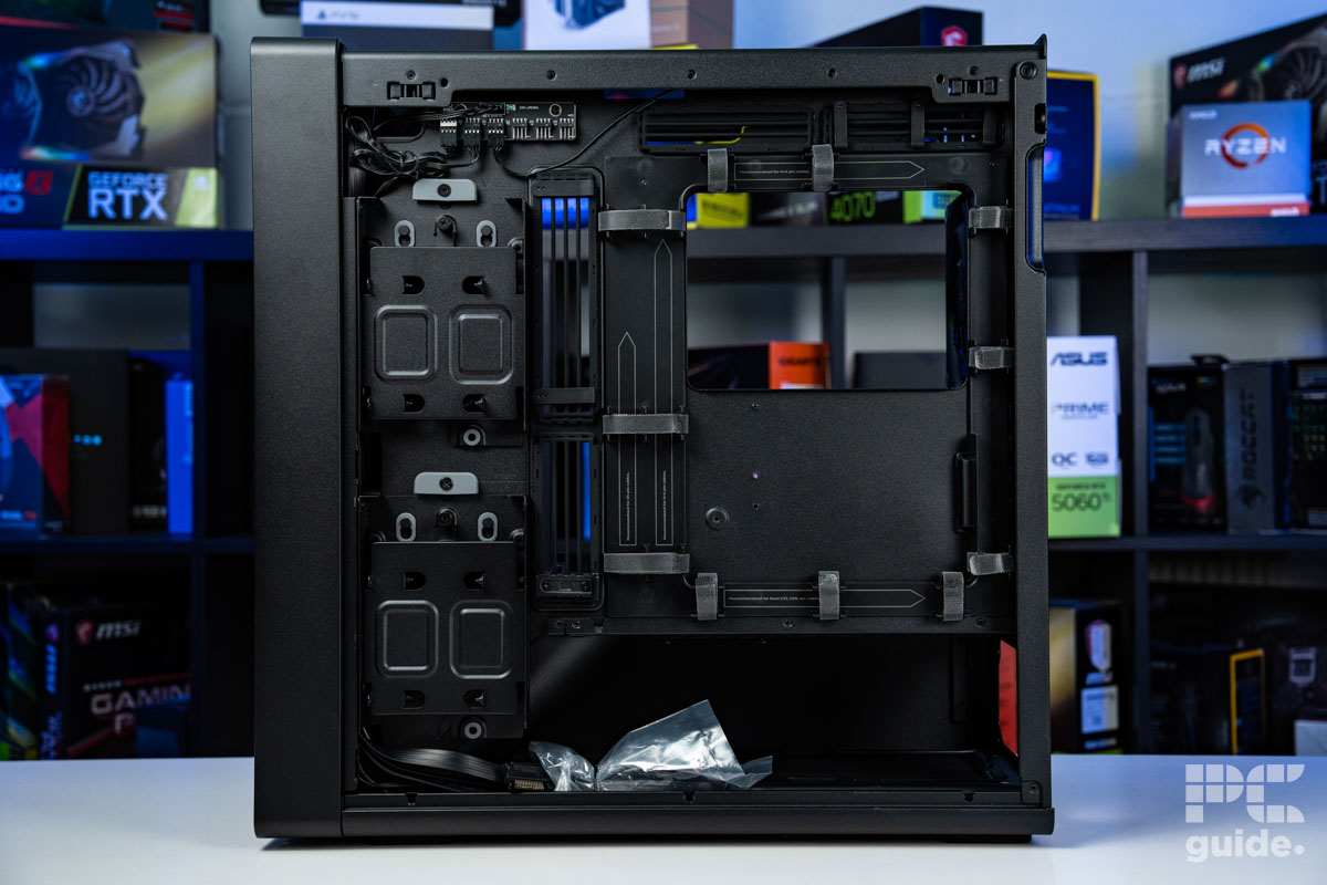 The left side open of the HAVN BF 360 Flowstanding on a white table infront of a bookshelf of PC component boxes. It shows the various stroage sleds, cable cahnnels and features of the case.
