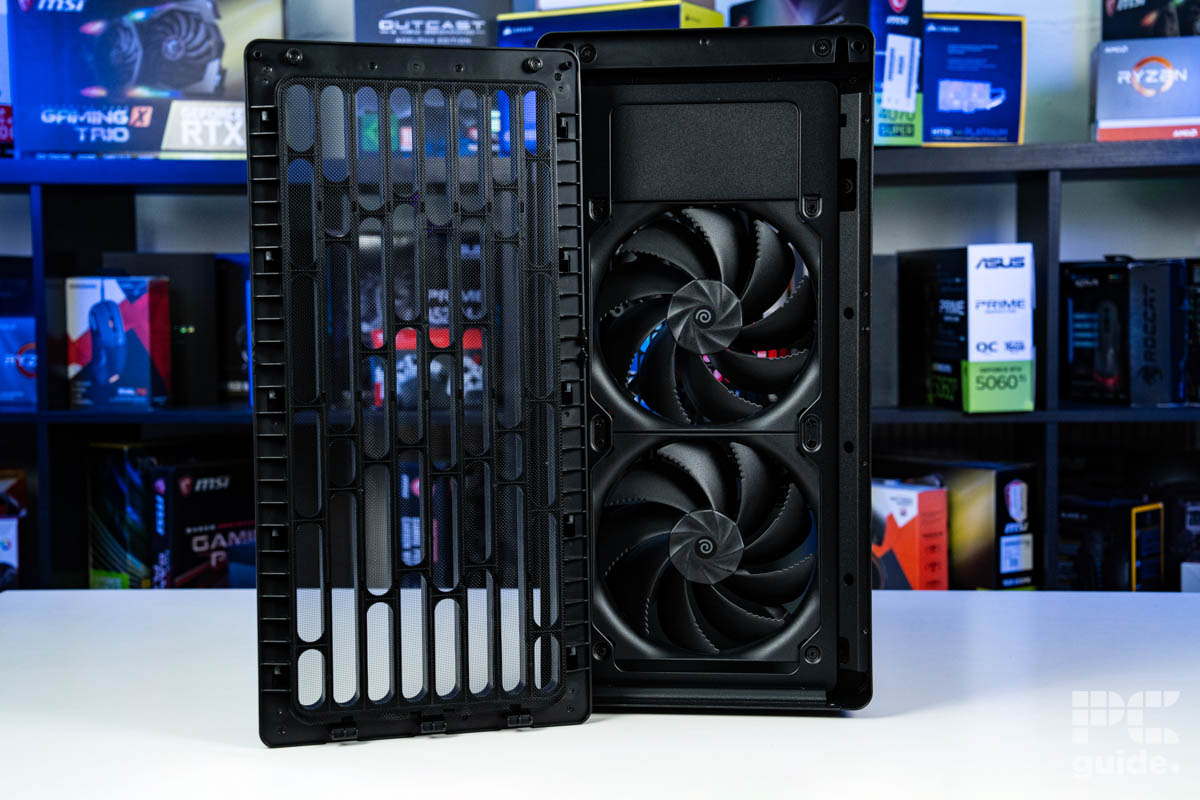 A shot of the front of the HAVN BF 360 Flow with its front panel taken off, it shows the two big 180mm fans in front. It stands on a white table with a background of a PC component boxes on a bookshelf.