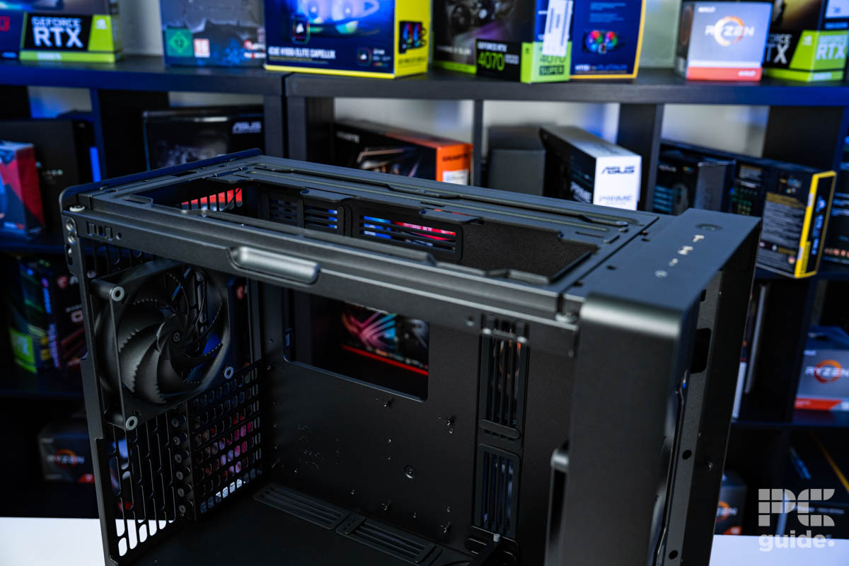 A shot of the top of the HAVN BF 360 Flow case with its panels off. It shows the fan mounting places with a background of PC component boxes on a bookshelf.