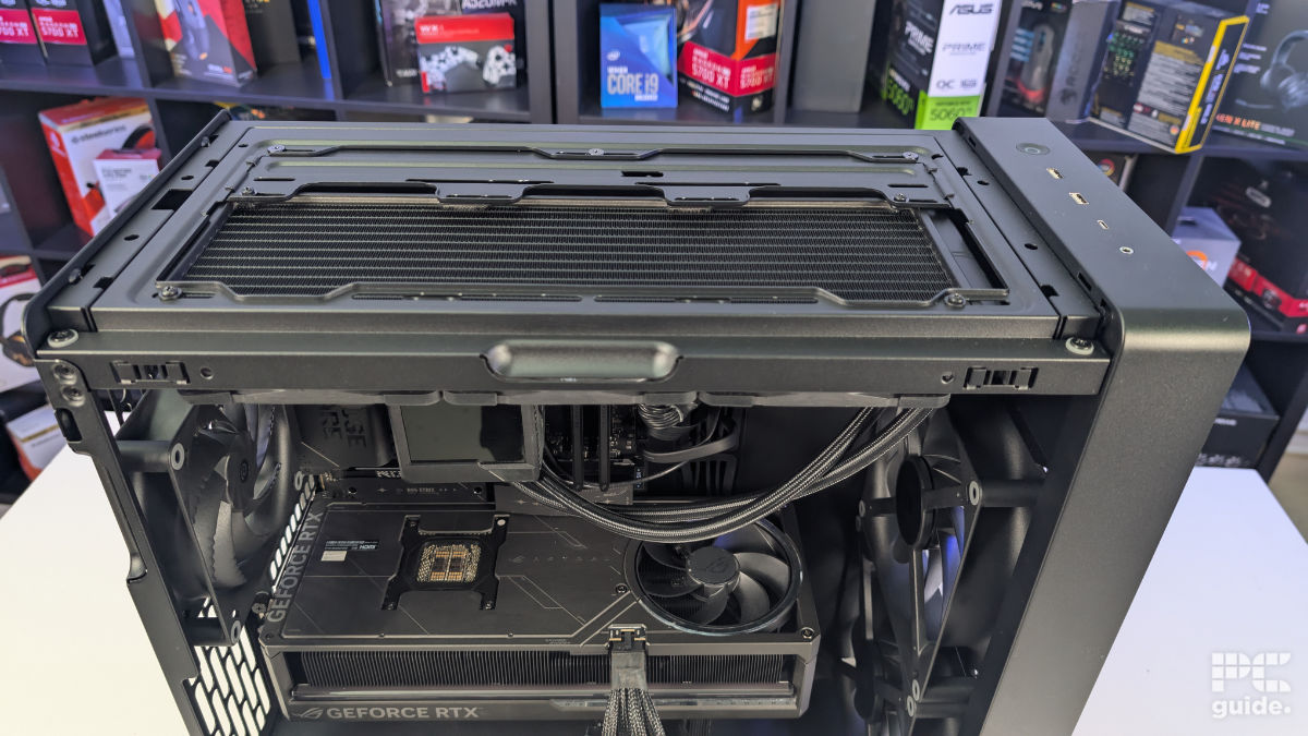 A top down view of the HAVN BF 360 case with the top taken off and a radiator underneath. With the inside built wihth PC components, standing on a white desk with a background of PC component boxes on a bookshelf.