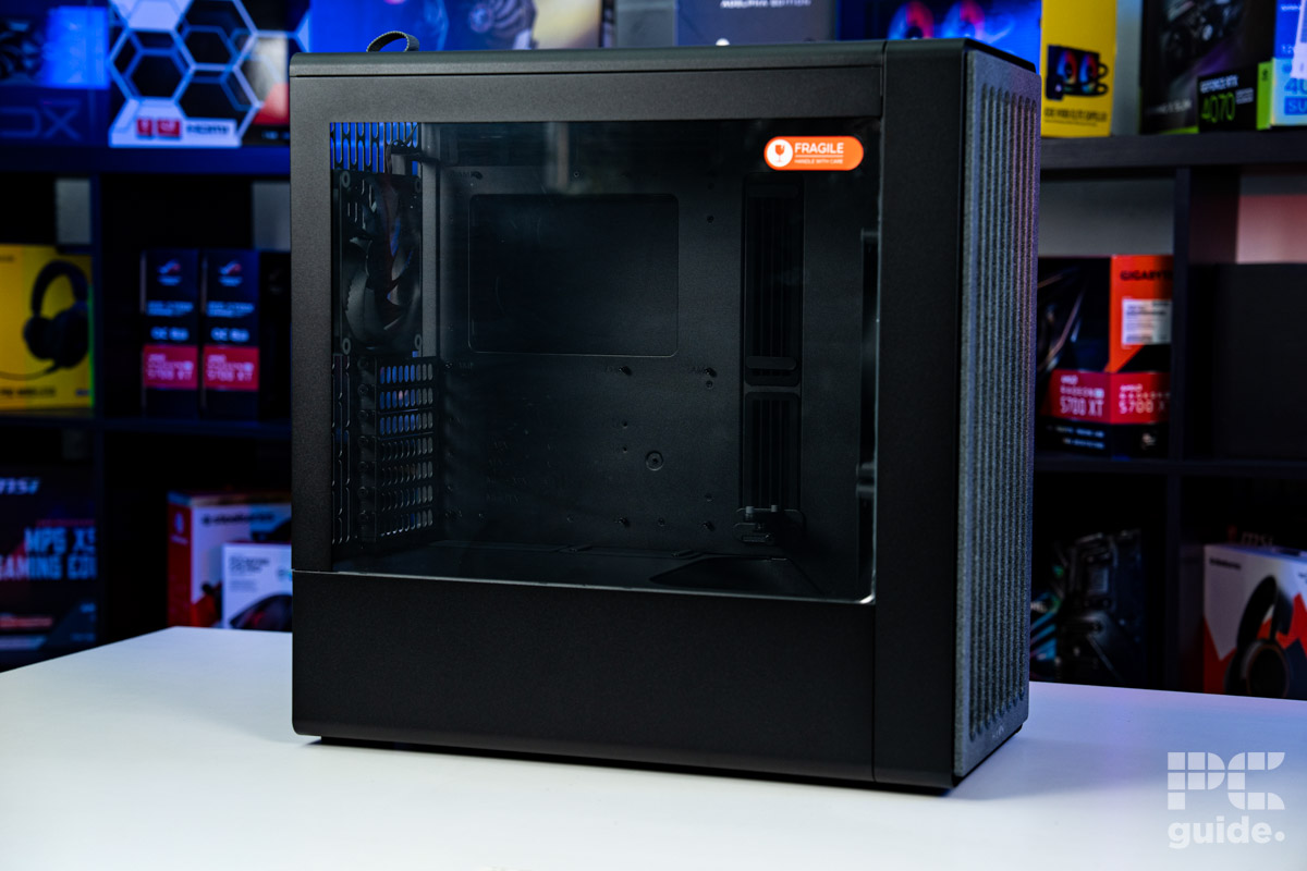 The HAVN BF 360 Flow case sitting side on with the right galss panel facing us. It sits on a white table with a background of PC component boxes on a bookshelf.