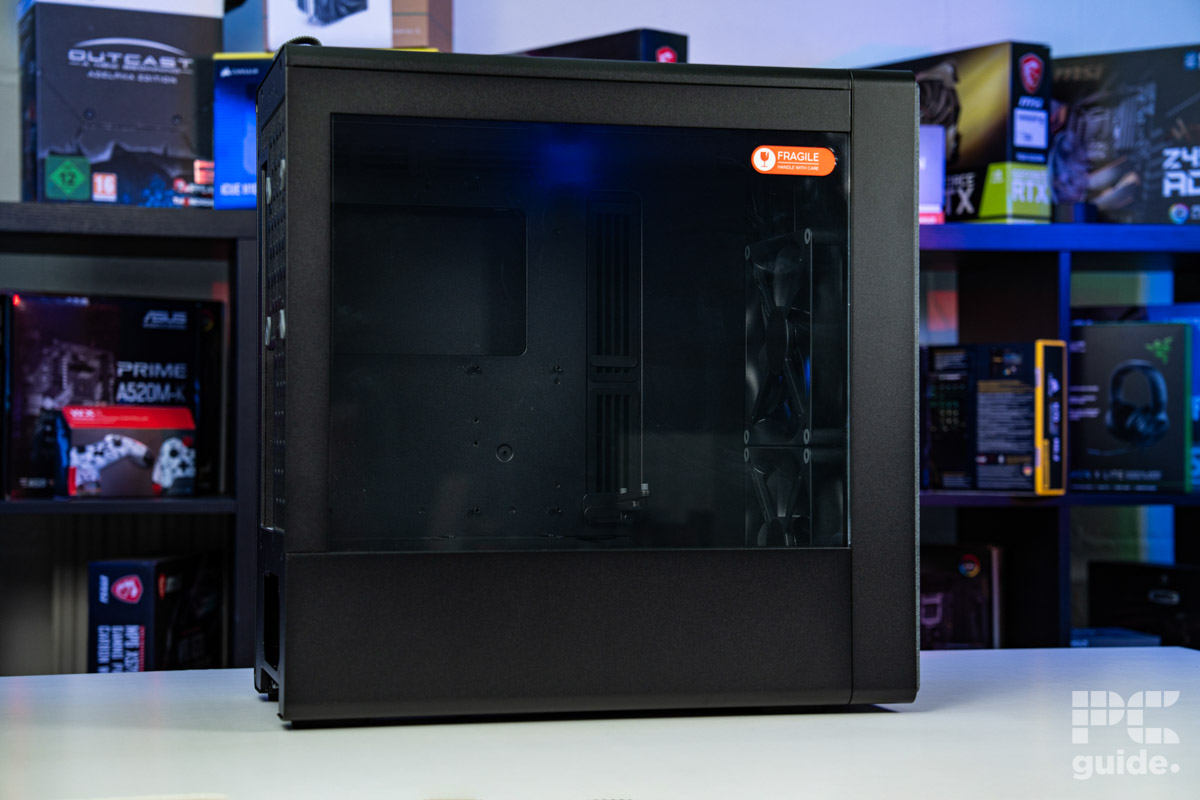 The HAVN BF 360 Flow case sitting side on with the right galss panel facing us. It sits on a white table with a background of PC component boxes on a bookshelf.