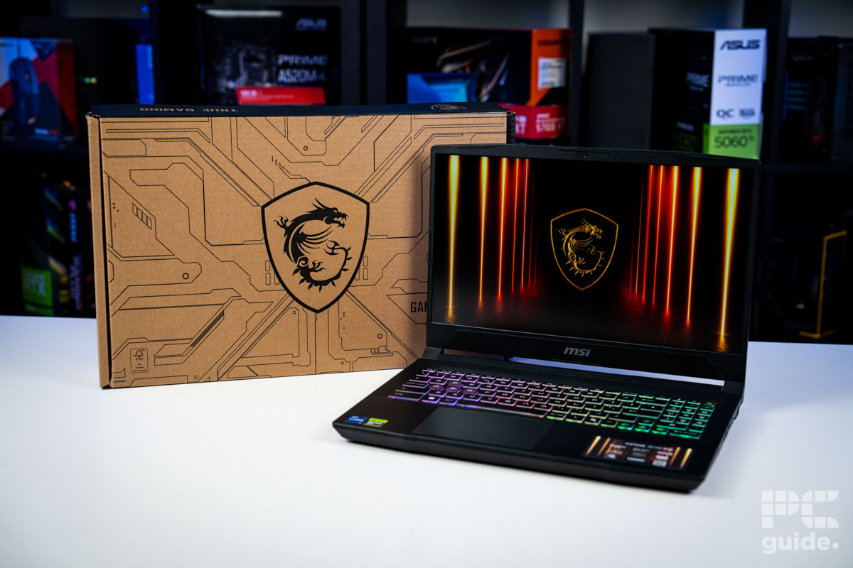 The MSI Katana 15 HX sitting on a white table with its box behind it and a background of a bookshelf full of PC component boxes.