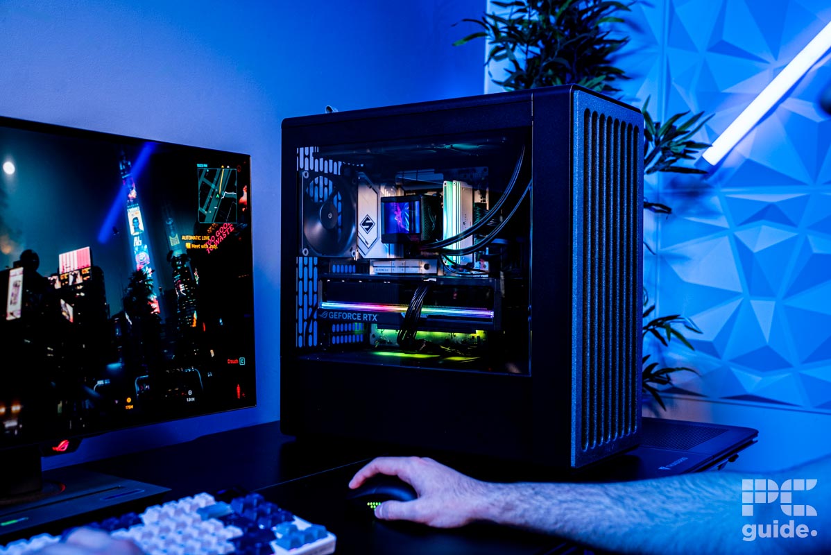 The HAVN BF 360 Flow case build sitting on a table showing its components. Next to it is a mouse, keyboard, and monitor with someones arm on the mouse playing Cyberpunk 2077 on the monitor.