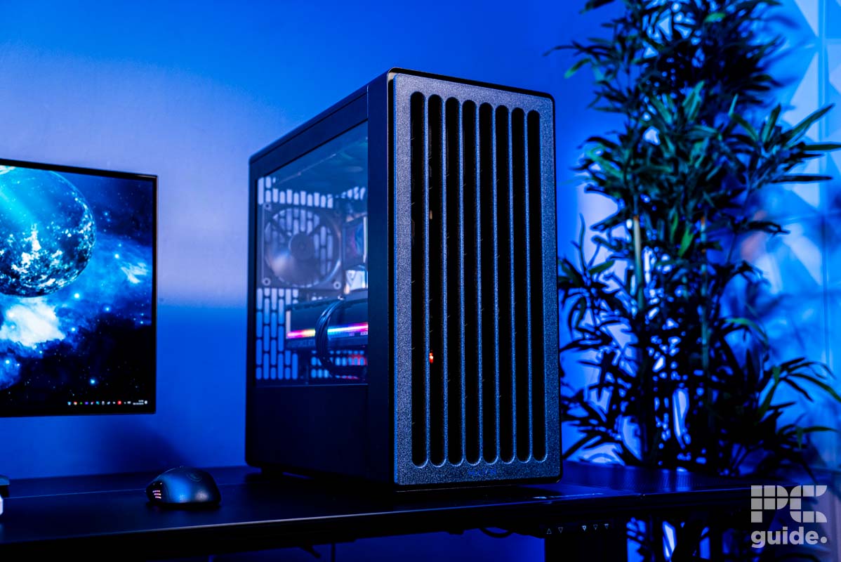 The front of the HAVN BF 360 Flow case at an angle sitting on a table. On the lkeft is a monitor and mouse, on the right is a tall plant, with a background of a blue wall.